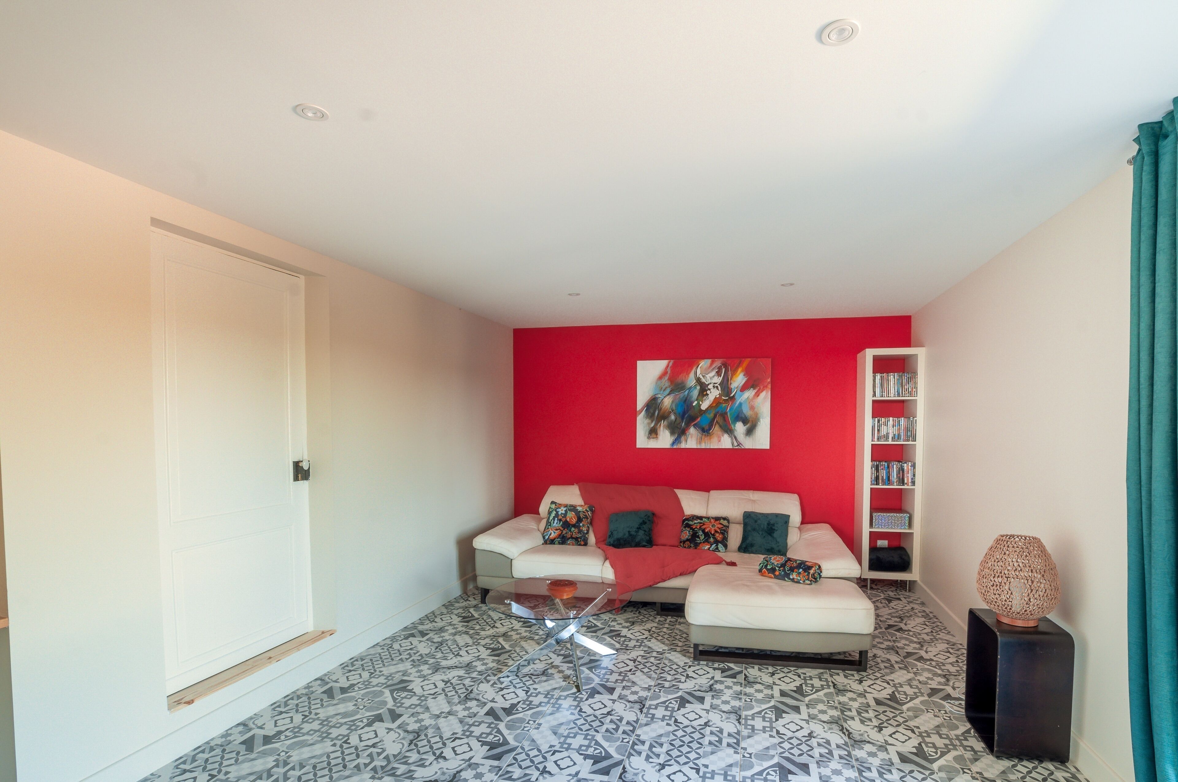 A modern living room with a red accent wall, a white sofa, a coffee table, and a bookshelf.