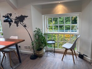 A modern room with a dining table, chairs, a world map on the wall, a large window with a view of trees, and a potted plant. - Lovely Riverside Perthshire Flat - Sleeps 8 (Blairgowrie)