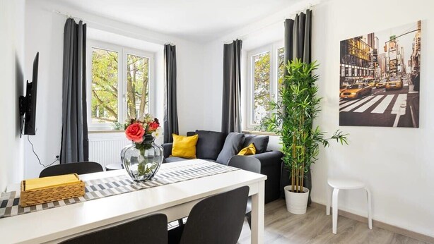 A modern living room with a sofa, a dining table, and a potted plant. - Apartment an der Theresienwiese (München)
