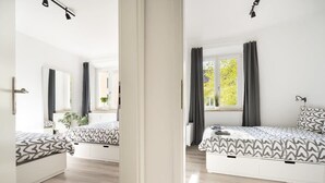 A modern bedroom with two beds, a large window with curtains, and a view of trees outside. - Apartment an der Theresienwiese (München)