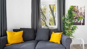 A grey sofa with two yellow cushions, a white chair, and a plant. - Apartment an der Theresienwiese (München)