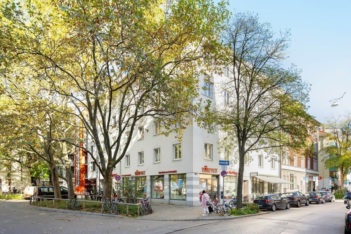 En gatubild med en rad träd, parkerade bilar och en byggnad med en butikslokal.