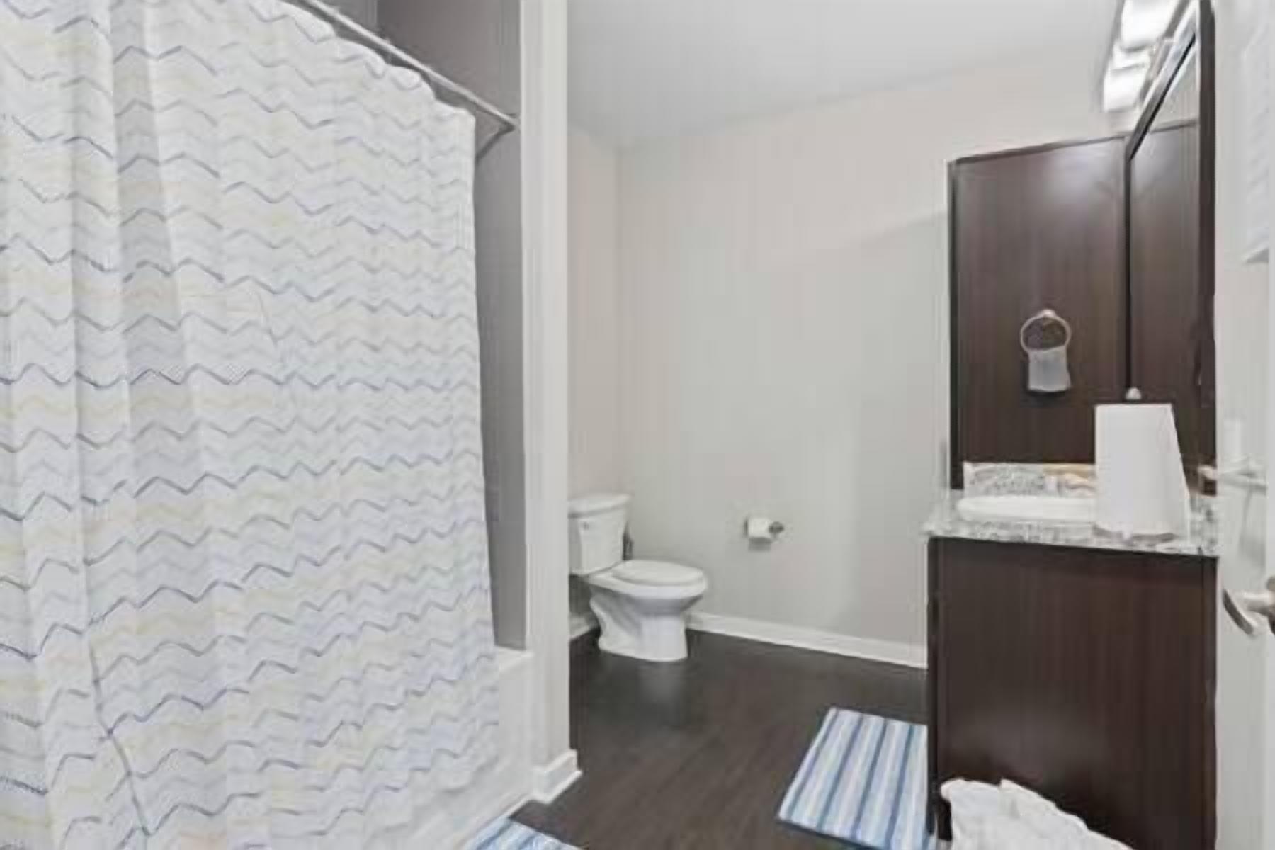 A bathroom with a shower curtain, toilet, and a vanity with a mirror.