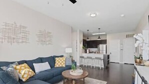 Uma sala de estar moderna com um sofá, mesa de centro e uma cozinha ao fundo.