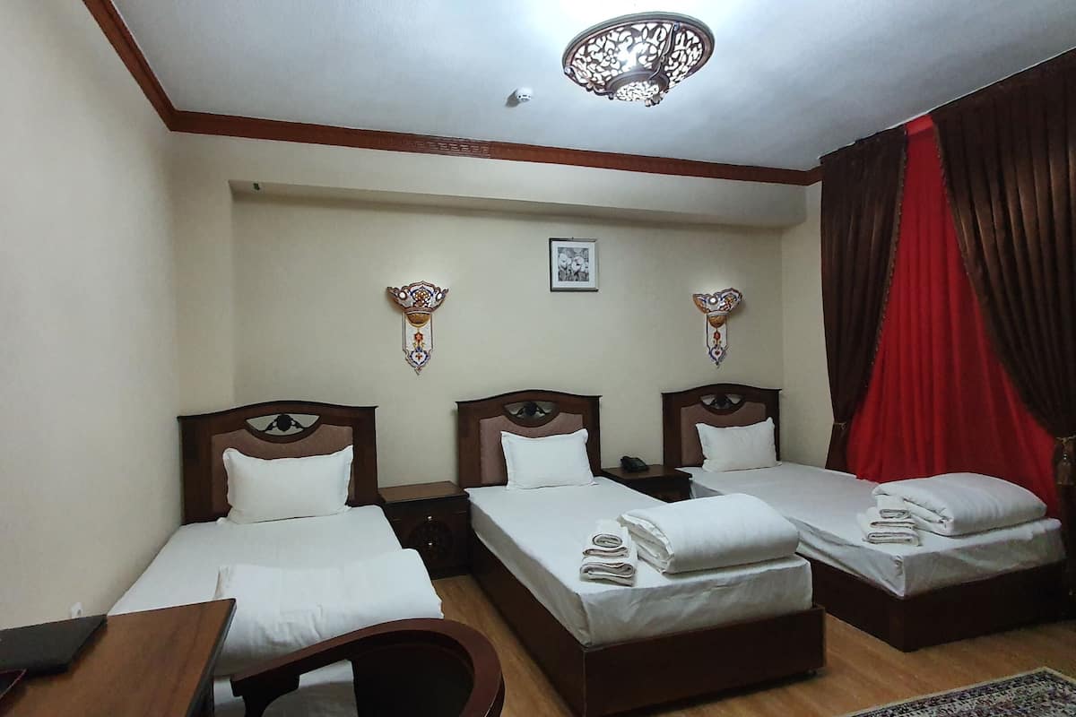 A hotel room with three single beds, a wooden desk, a chair, a small table, and a ceiling light fixture.