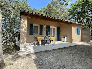 Un petit bâtiment avec un toit en tuiles, un patio couvert avec une table et des chaises, et une porte avec des volets bleus.