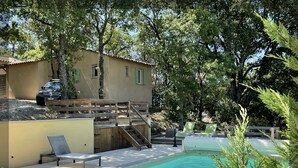 A pool area with lounge chairs, a wooden deck, and a building with a car parked outside.