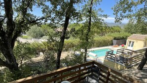 A wooden deck with a table and chairs, overlooking a swimming pool and a house.