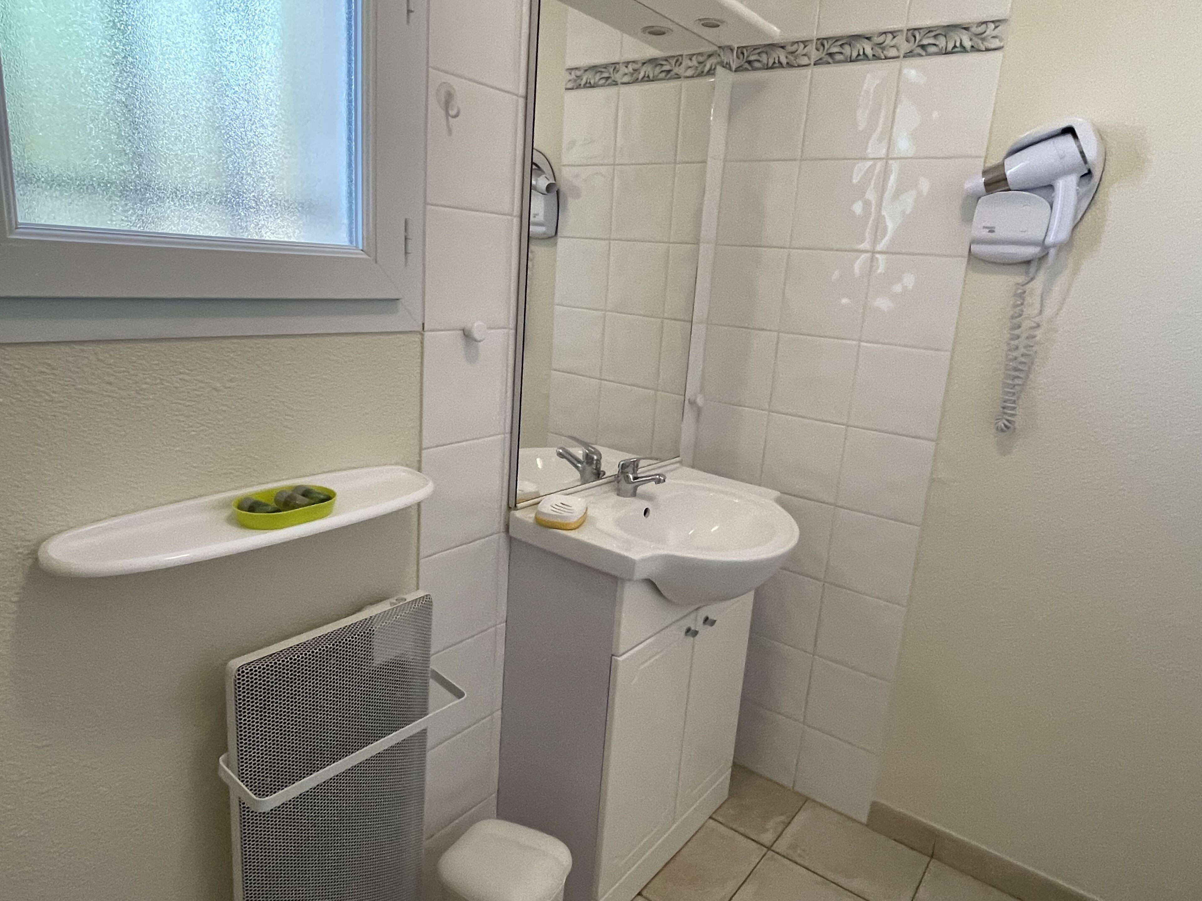 Une salle de bain équipée d’un lavabo, d’un miroir et d’un sèche-cheveux fixé au mur.