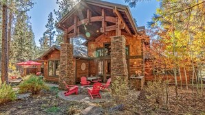 A log cabin with a stone foundation, a covered patio with red Adirondack chairs, and a dining area with a red umbrella. - AC, gourmet kitchen, pet friendly, Luxury (Sunriver)