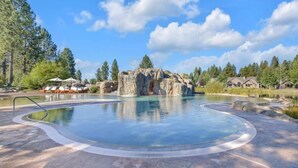A swimming pool with a natural rock formation, lounge chairs, and a clear sky. - AC, gourmet kitchen, pet friendly, Luxury (Sunriver)