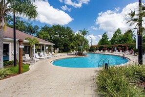 Un área de piscina con sillones reclinables y un edificio con tejado de baldosas.