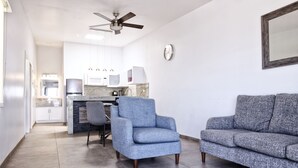 A modern living room with a grey sofa, a blue armchair, and a dining area with a kitchen in the background. - Popotla Villa 203 (PLAYAS DE ROSARITO)