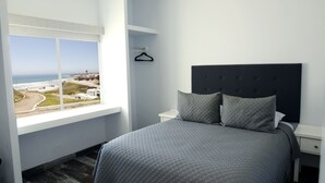 A bedroom with a large window offering a view of the beach and buildings. - Popotla Villa 203 (PLAYAS DE ROSARITO)