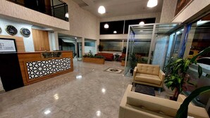 A lobby with a reception desk, seating area, and a glass elevator.