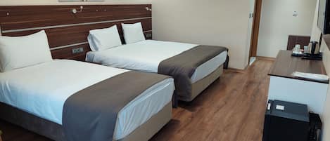A hotel room with two beds, a desk, a chair, a small table, and a kitchenette.