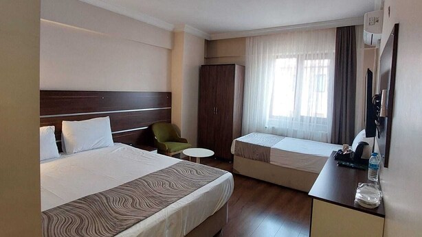 A hotel room with a large bed, a desk, a chair, a wardrobe, and a window with curtains.