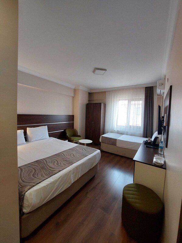 A hotel room with a large bed, a desk, a chair, a wardrobe, and a window with curtains.