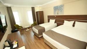 A hotel room with two beds, a desk with a tray of breakfast items, a green chair, a small table, and a painting on the wall.
