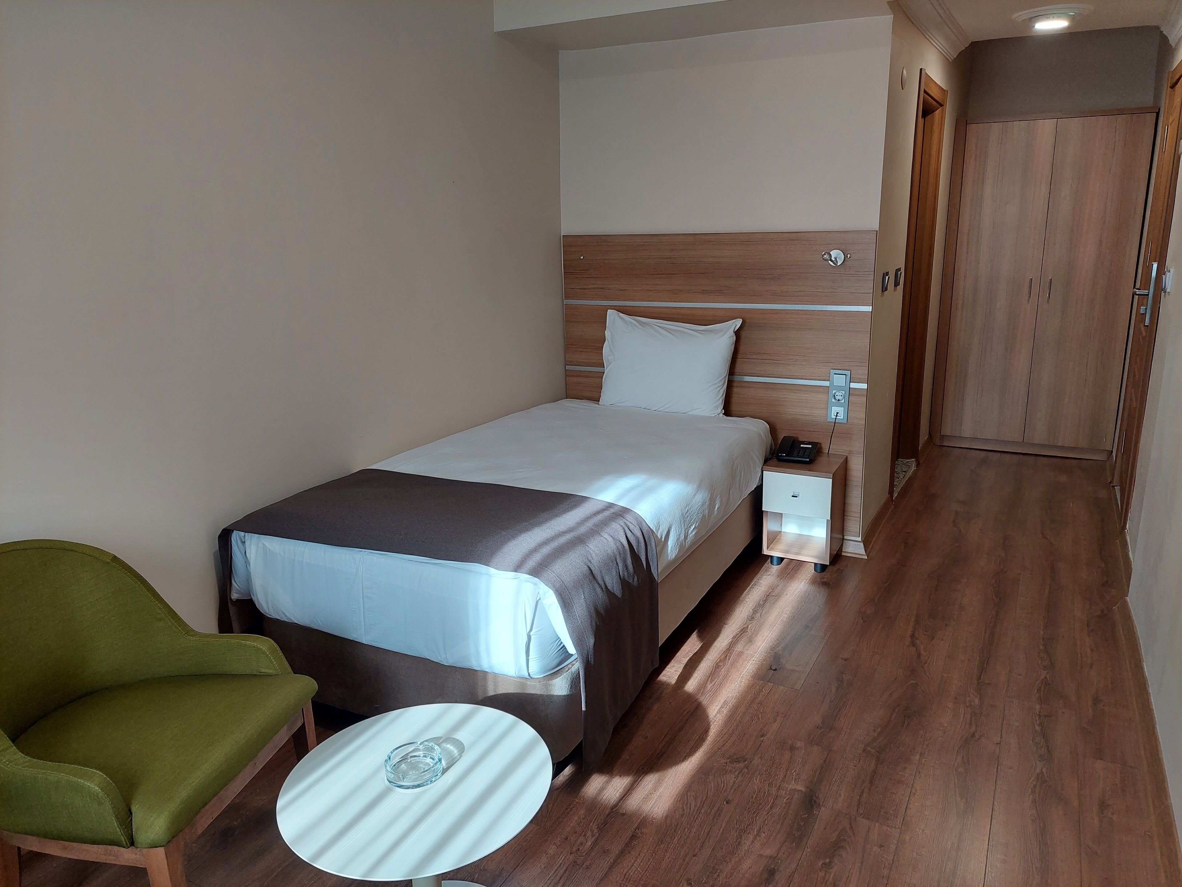 Hotellihuone, jossa on sänky, yöpöytä, lamppu, tuoli ja vaatekaappi.