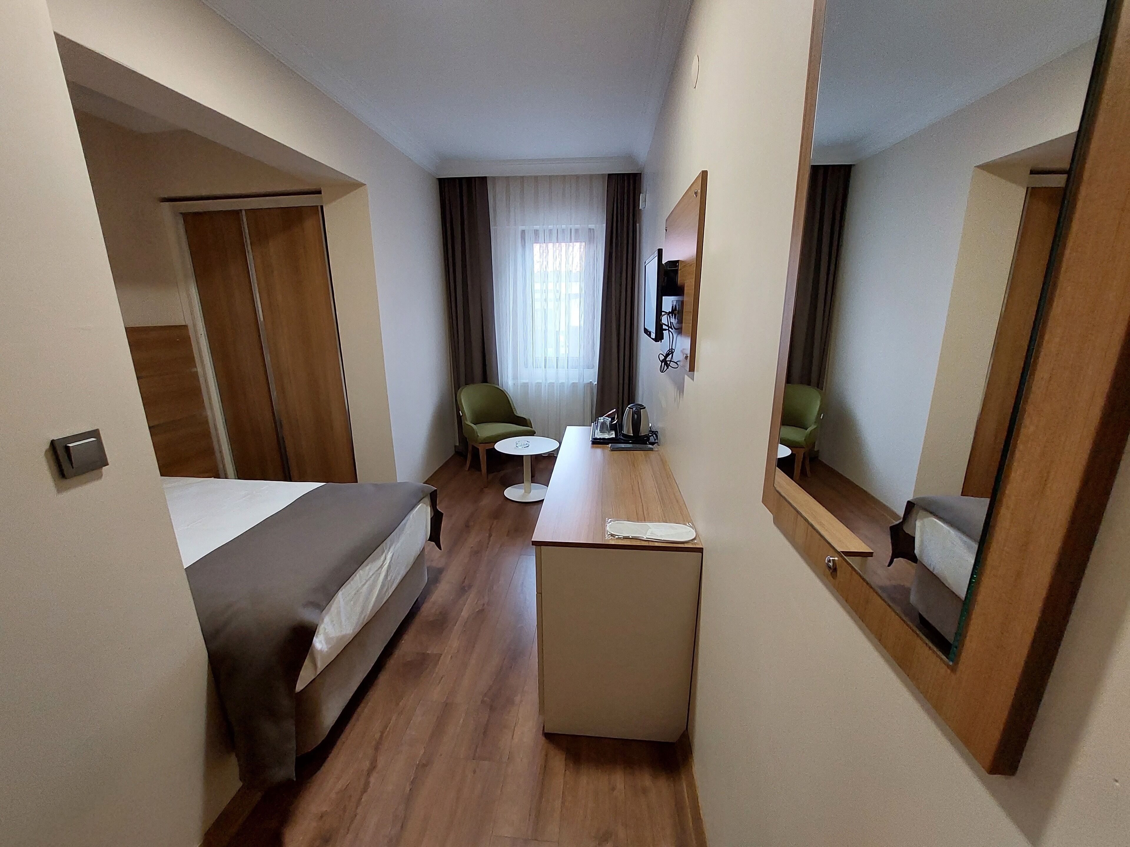 A hotel room with a bed, a desk, two chairs, a small table, a mirror, and a window with curtains.
