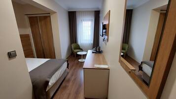 A hotel room with a bed, a desk, two chairs, a small table, a mirror, and a window with curtains.