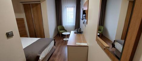 A hotel room with a bed, a desk, two chairs, a small table, a mirror, and a window with curtains.
