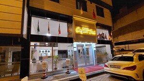 A hotel entrance with a neon sign, a car parked in front, and a cobblestone street. - Beyaz Inci Otel (Sivas)