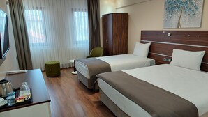 A hotel room with two beds, a desk with a kettle and cups, a green ottoman, and a painting on the wall. - Beyaz Inci Otel (Sivas)