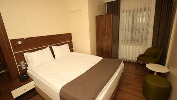 A hotel room with a large bed, a bedside table with a phone, a green ottoman, a small round table, and a chair.