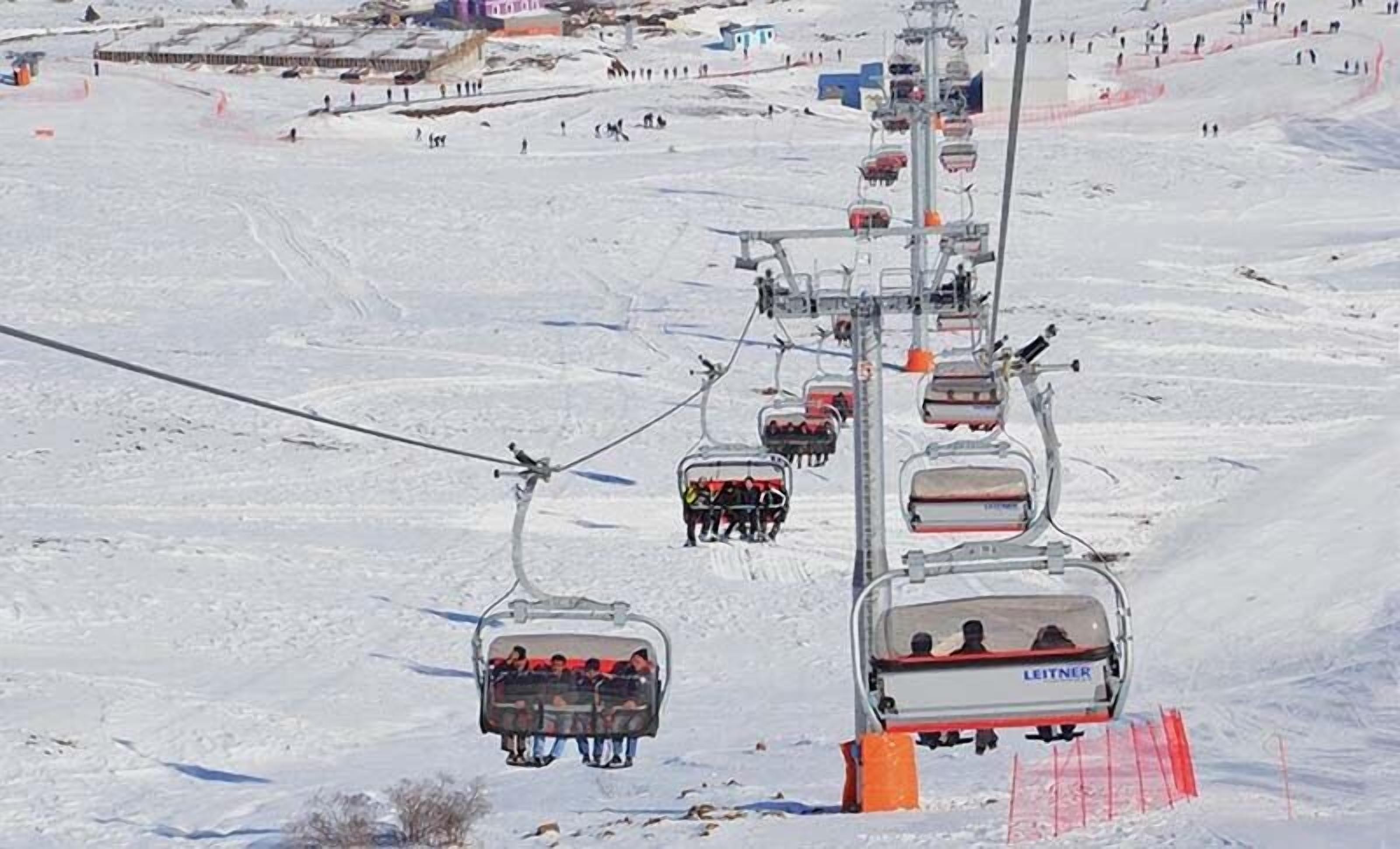 A ski lift system with multiple chairs ascending a snowy slope.