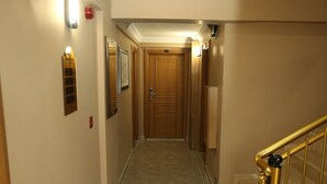 A hallway with a wooden door at the end, a light switch, and a wall-mounted light fixture. - Beyaz Inci Otel (Sivas)