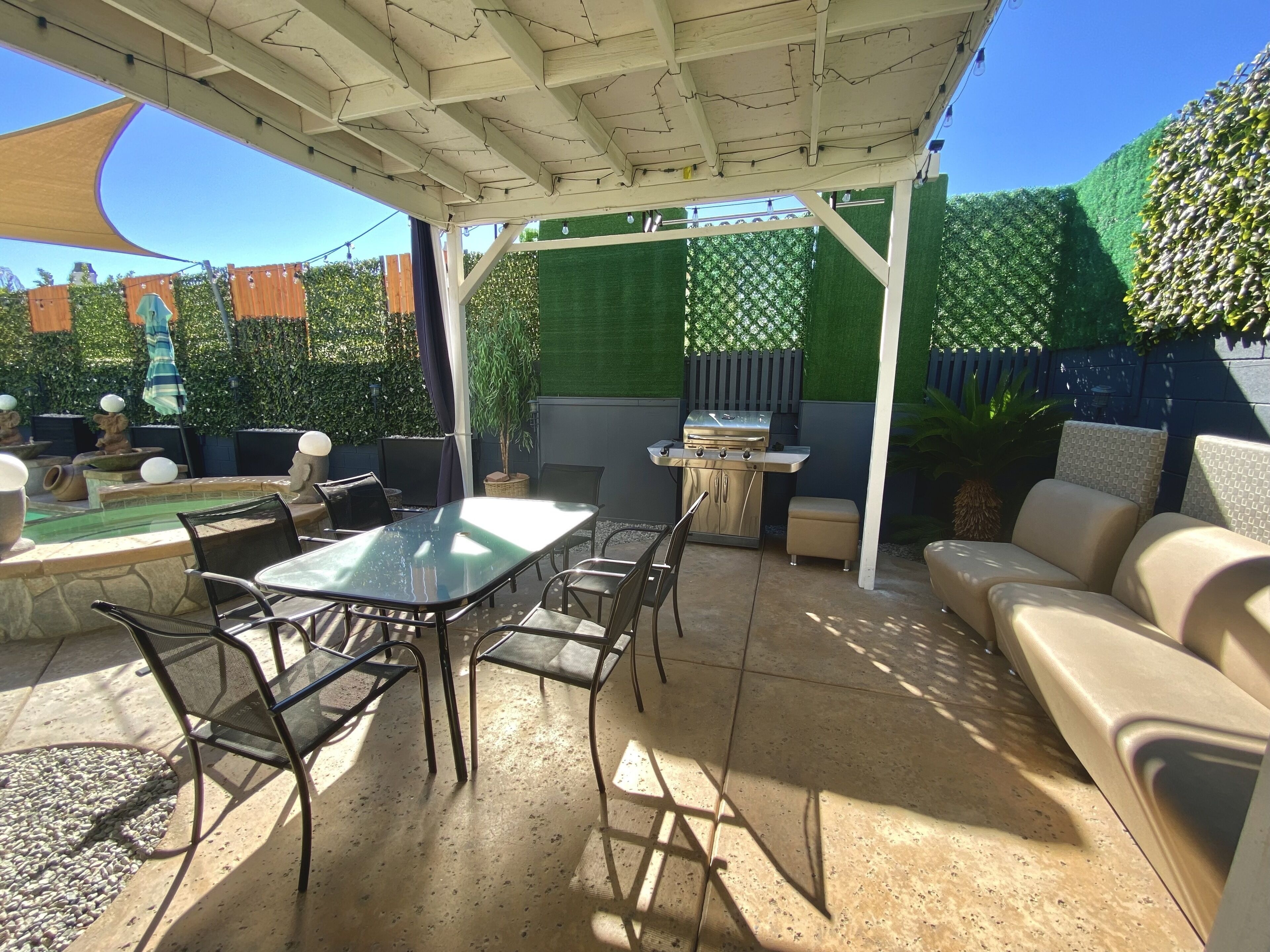 Un patio con mesa y sillas, una parrilla, una piscina y una zona de estar techada.