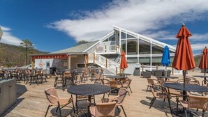 Une terrasse extérieure avec des tables et des chaises rondes, un espace piscine et un bâtiment sur lequel est affiché un panneau indiquant « BASE CAMP ».