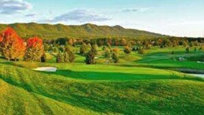Un parcours de golf avec des collines verdoyantes, des arbres aux feuilles d’automne et un ciel dégagé.