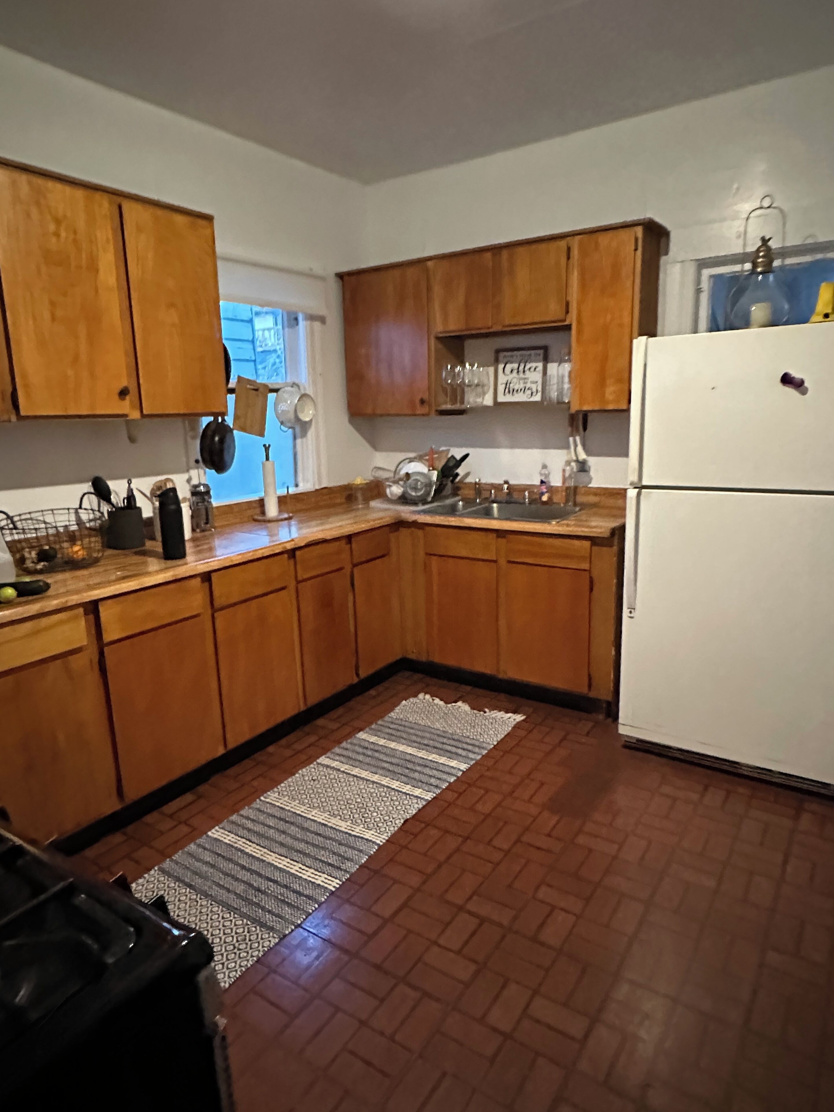 Eine Küche mit Holzausstattung, einem weißen Kühlschrank, einer Spüle und einem gemusterten Teppich.