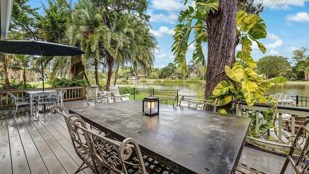 An outdoor patio with a table and chairs, surrounded by tropical plants and a view of a lake. - Lakeside Retreat |Private Pool| 8min walk Downtown (Saint Augustine)