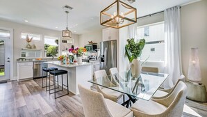 A modern kitchen with a glass dining table, bar stools, and pendant lighting. - LUX Riberia – 315 | 12-min walk to Historic DTN (St. Augustine)