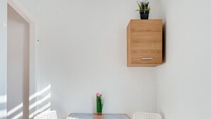 Une pièce moderne et minimaliste, avec une table en bois, deux chaises blanches, une petite plante en pot et un radiateur blanc.