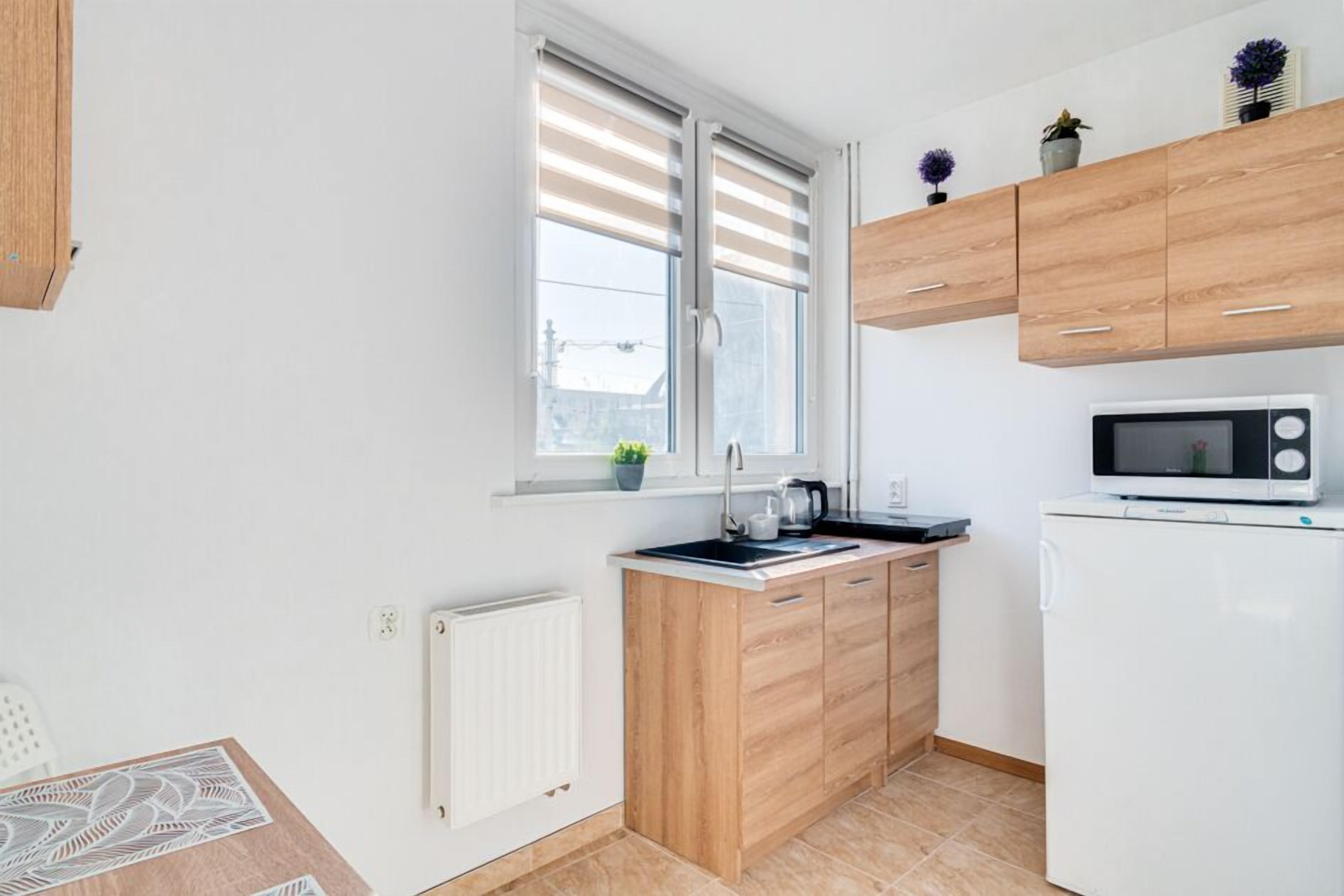 Una cucina compatta con mobili in legno, un frigorifero bianco, un forno a microonde e una finestra con persiane.