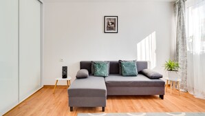 Un salon moderne avec un canapé d’angle gris, une petite table d’appoint, une plante en pot et un tableau encadré accroché au mur.