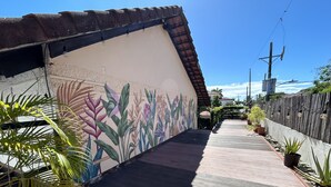 Un étroit sentier en bois, bordé de plantes en pot et agrémenté d’une fresque colorée.