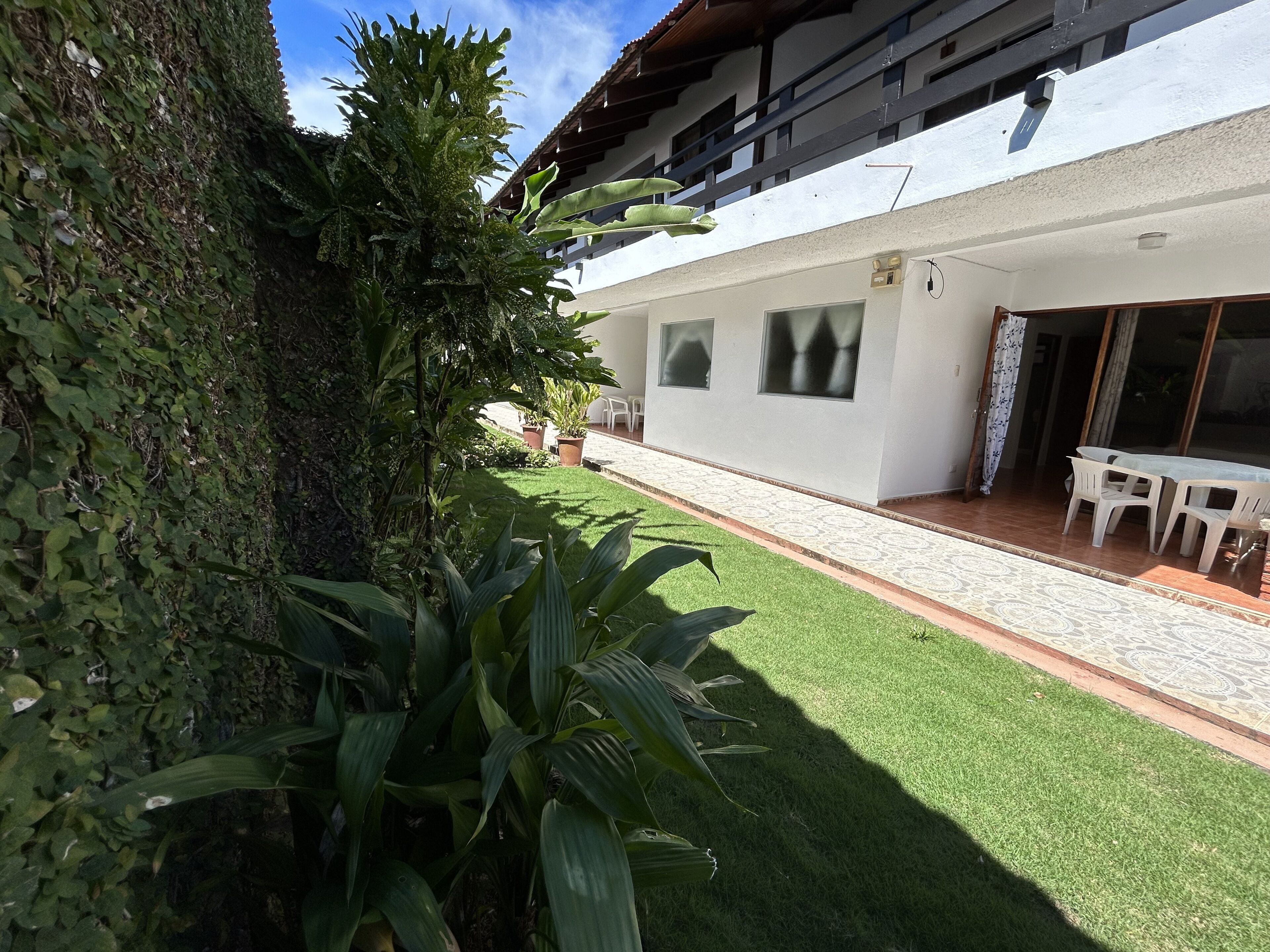 A modern building with a white exterior, a covered patio with white plastic chairs, and a well-maintained lawn.