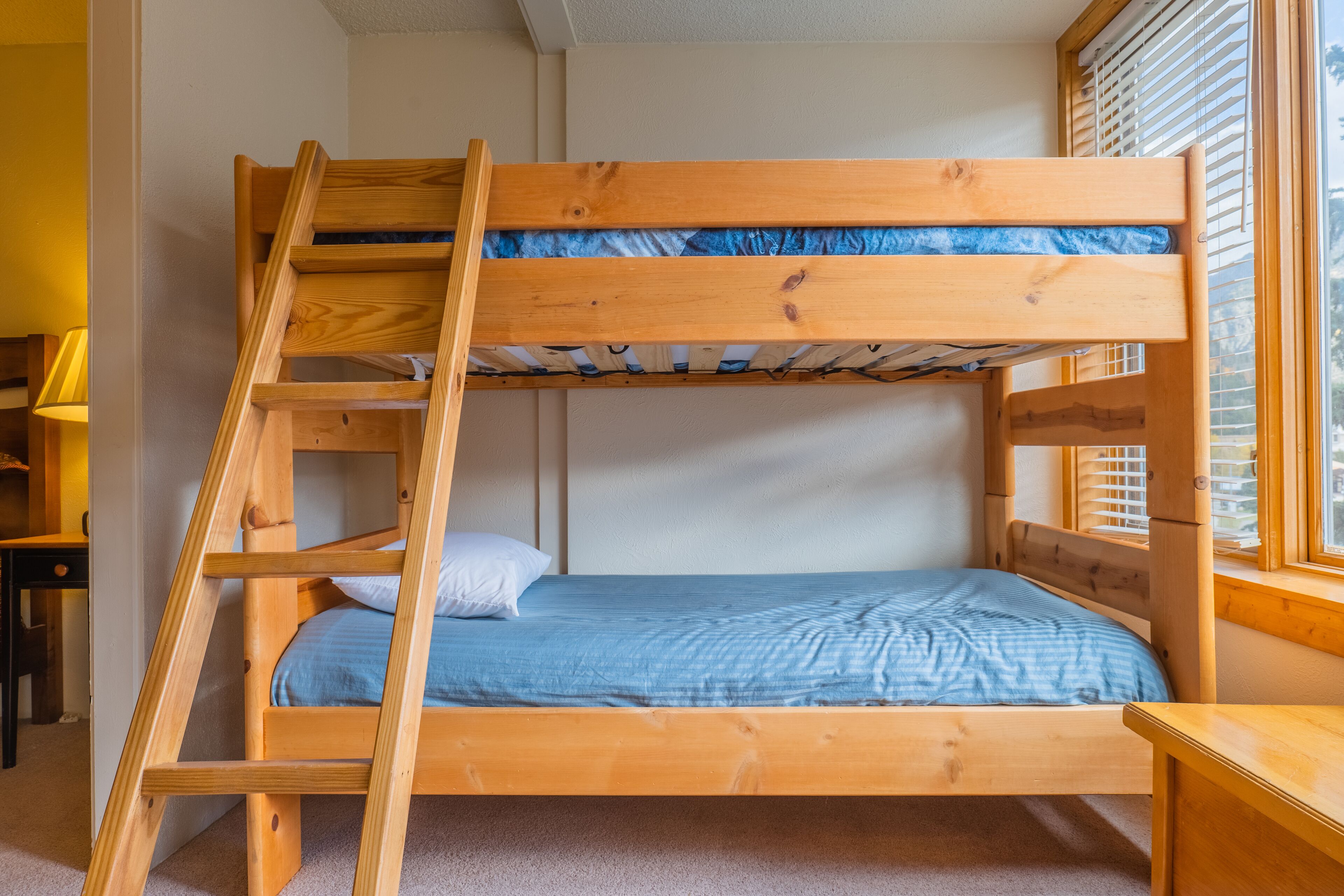 Una cama litera con escalera de madera, un escritorio y una ventana con persianas.