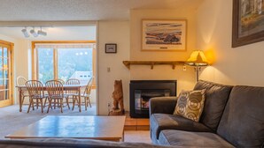A cozy living room with a fireplace, a dining area with wooden chairs, and a sofa with patterned cushions. - Spacious Condo, Short Walk to Lifts. SH301 (Copper Mountain)