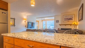 A kitchen with granite countertops, wooden cabinets, a dining area with chairs, and a large window providing a view. - Spacious Condo, Short Walk to Lifts. SH301 (Copper Mountain)