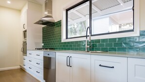 A modern kitchen with white cabinetry, a green-tiled backsplash, and a window above the sink. - Off grid luxury space in Central West NSW (Forest Reefs)