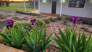 A house with a covered porch, a garden with flowers, and a field in the background. - Off grid luxury space in Central West NSW (Forest Reefs)