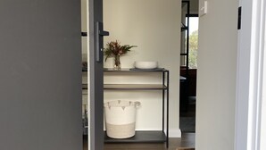 A narrow hallway with a wooden floor, a black metal shelf unit with a bowl and a plant, and a white door frame. - Off grid luxury space in Central West NSW (Forest Reefs)