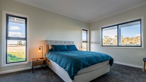 A bedroom with a large bed, two bedside tables, and two windows offering a view of the outdoors. - Off grid luxury space in Central West NSW (Forest Reefs)